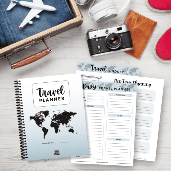 The Clutter Keeper travel planner and three planning pages on a desk with a suitcase